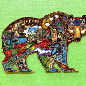 May include: A colorful bear-shaped patch with intricate designs. The bear is filled with images of nature, including fish, an eagle, and mountains. The patch is set against a light green background.