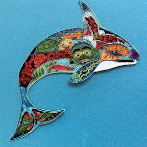 May include: A colorful, hand-painted orca whale with a detailed design featuring a butterfly, sea creatures, and a human face. The orca is on a blue background.