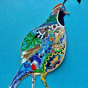 May include: A colorful, hand-painted, paper cut-out of a quail with intricate details and patterns. The bird is standing on a blue background.