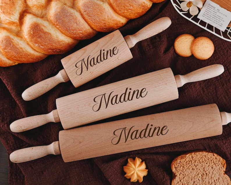 Pu&ograve; includere: Tre mattarelli di legno con il nome "Nadine" inciso su di essi. I mattarelli sono di dimensioni diverse e sono disposti su una superficie di tessuto marrone.