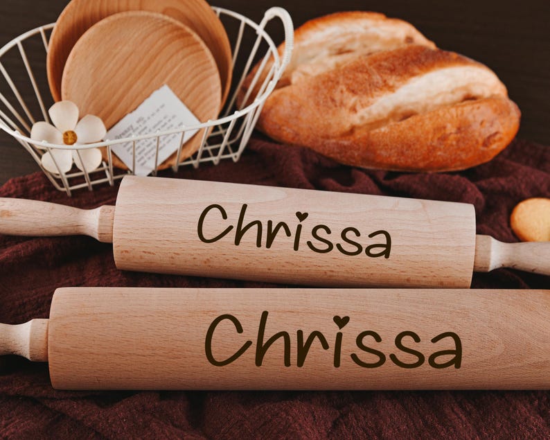 Pu&ograve; includere: Due mattarelli di legno con il nome "Chrissa" inciso su di essi. I mattarelli sono su una superficie marrone.