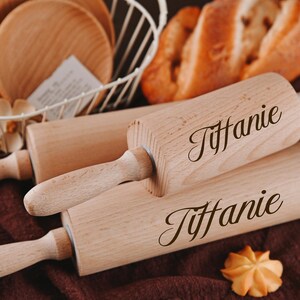 Pu&ograve; includere: Due mattarelli di legno con il nome "Tiffanie" inciso su di essi. I mattarelli sono su una superficie marrone con un pane e un cesto di filo metallico bianco sullo sfondo.