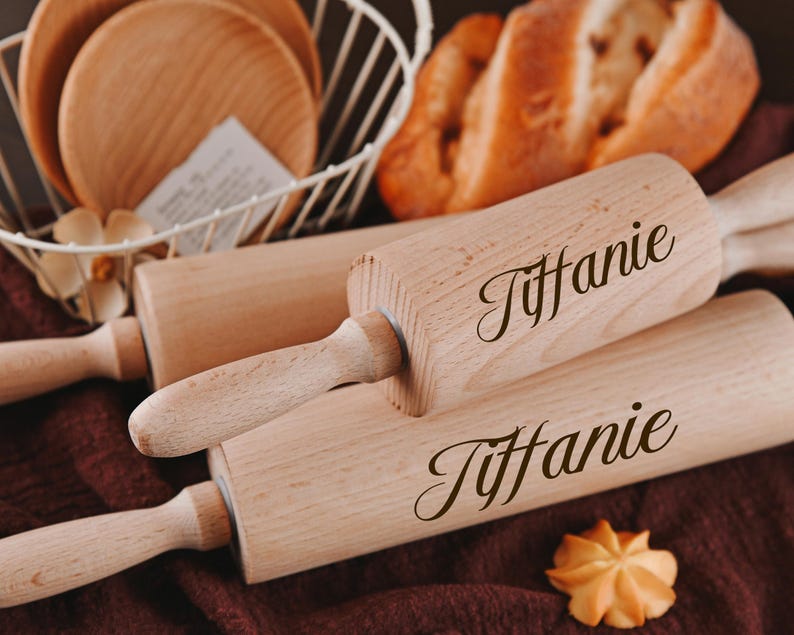 Pu&ograve; includere: Due mattarelli di legno con il nome "Tiffanie" inciso su di essi. I mattarelli sono su una superficie marrone con un pane e un cesto di filo metallico bianco sullo sfondo.