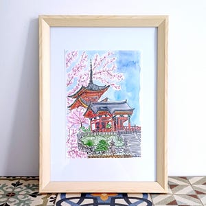 May include: A watercolor painting of a red Japanese temple with a cherry blossom tree in the foreground. The temple has a tiered roof and is surrounded by green foliage. The painting is framed in a light wood frame.