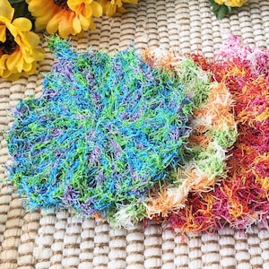 May include: Five colorful crocheted scrubbers in shades of green, blue, orange, pink, and black. The scrubbers are made of soft, fluffy yarn and are perfect for cleaning dishes or other surfaces.