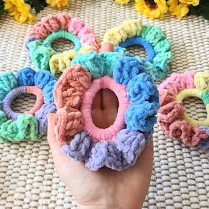 May include: A set of five colorful crocheted hair scrunchies in pastel shades of pink, blue, green, and yellow. The scrunchies are made with a soft, fuzzy yarn and have a gathered, ruffled texture.