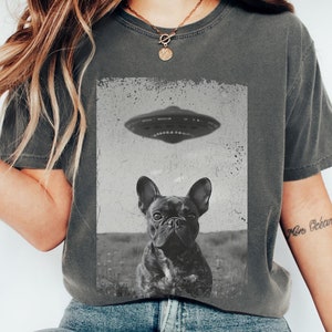 Könnte beinhalten: Eine Frau trägt ein graues T-Shirt mit einer Schwarzweißgrafik eines französischen Bulldoggen, der zu einem fliegenden Untertasse schaut. Der Text "Pepper" befindet sich in der oberen rechten Ecke des Bildes.