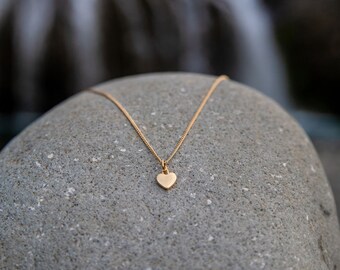May include: A gold heart pendant necklace on a gray stone background.