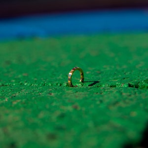 May include: A gold ring with small colorful stones set into the band. The ring is lying on a green surface.
