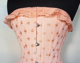 May include: A peach-colored corset with a floral pattern and a lace trim. The corset has a structured design with metal clasps down the front. The fabric has a subtle sheen, and the overall aesthetic is vintage-inspired.