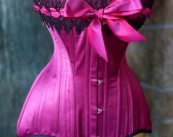May include: A magenta satin corset with black lace trim and a large magenta satin bow. The corset has a pointed bottom and is fastened with silver buttons.