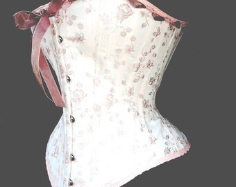 May include: A white corset with a floral pattern and a pink ribbon bow. The corset has a lace trim and is made of a satin-like fabric.