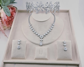 May include: A silver bridal jewellery set comprising a tiara, necklace, earrings, and bracelet, displayed on a beige tray. The tiara and necklace feature a floral design, while the earrings and bracelet are embellished with sparkling stones.