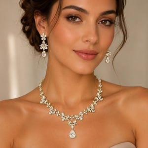 May include: A gold-toned necklace and matching drop earrings set featuring clear, faceted, marquise-cut stones arranged in floral patterns. The necklace includes a central pear-shaped stone pendant, while the earrings feature a similar floral design.