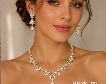 May include: A gold-toned necklace and matching drop earrings set featuring clear, faceted, pear-shaped and floral-shaped crystals. The necklace has a central pear-shaped pendant, while the earrings feature a floral stud with a drop.