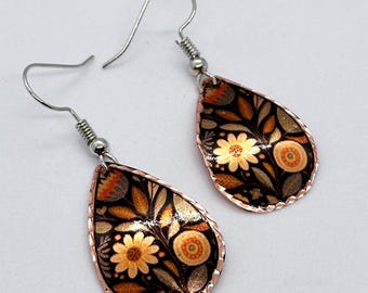 Puede incluir: Un par de pendientes en forma de lágrima con un patrón floral. Los pendientes están hechos de cobre y tienen un gancho de plata.