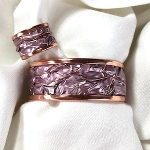 Op de afbeelding: Een set van twee koperen armbanden met een gehamerde, textuur en een paarse, iriserende coating.
