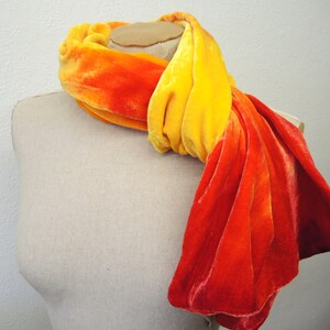 May include: A long, ombre scarf in shades of orange and yellow. The scarf is made of a soft, velvety fabric and is draped over a mannequin's neck.