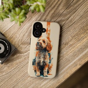 May include: A phone case featuring a watercolor-style illustration of a dog. The case has a cream-colored background with orange and blue accents. The dog is depicted with brown and cream fur.