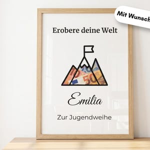 May include: A framed print with the text "Erobere deine Welt" and "Emilia" in black script. The artwork features a mountain graphic with a flag at the peak, filled with colorful currency. The phrase "Zur Jugendweihe" is also included.