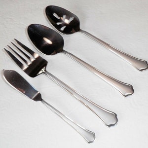 May include: A set of four silver-toned utensils, including a butter knife, a fork, a slotted spoon, and a regular spoon. The utensils have a simple, elegant design with a rounded handle.