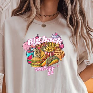 May include: A beige t-shirt with a graphic print of various fast food items and the text "Big back energy" in pink.