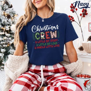 May include: Navy blue t-shirt with the text "Christmas CREW" in white and red. The shirt also has the phrases "a little bit crazy", "a little bit loud", and "a whole lotta love". The model is wearing red and white plaid pajama pants.