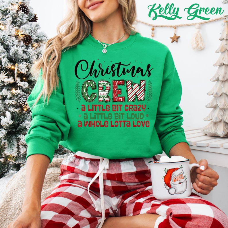 May include: A Kelly Green Christmas Crew sweatshirt with the text "Christmas Crew" in black and red. The sweatshirt also has the phrases "a little bit crazy", "a little bit loud", and "a whole lotta love". The person is wearing red and white plaid pajama pants.