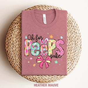 May include: A heather mauve t-shirt with the text "Oh for Peeps sake" in colorful letters with a bunny and Easter egg designs.
