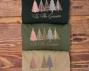 May include: Three sweatshirts in different colors, forest green, military green, and cream/tan, with a design of five stylized Christmas trees and the text 'Tis The Season'.
