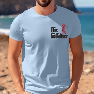 May include: A light blue t-shirt with a black and red graphic of a golfer and the text "The Golfather".