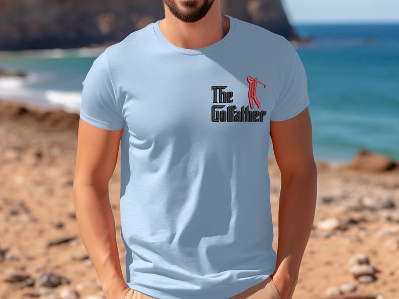 May include: A light blue t-shirt with a black and red graphic of a golfer and the text "The Golfather".