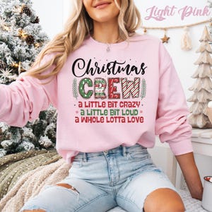 May include: A light pink sweatshirt with the text "Christmas CREW" in black and red. The word "CREW" is decorated with green and red patterns. Below the main text are the phrases "a LITTLE BIT CRAZY", "a LITTLE BIT LOUD", and "a WHOLE LOTTA LOVE".
