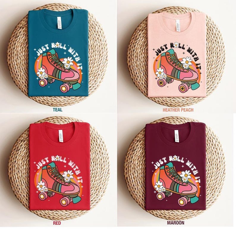 May include: Four t-shirts in teal, heather peach, red, and maroon colors. Each shirt features a graphic of a pink roller skate with white daisies, a rainbow arc, and the text "JUST ROLL WITH IT" printed in a white, curved font.