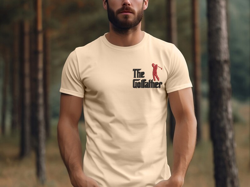 May include: A beige t-shirt with a black and red graphic that says "The Golfather" with a golfer silhouette.