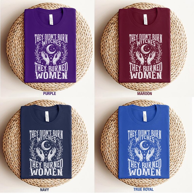 May include: Four t-shirts in purple, maroon, navy, and true royal blue, each with the text "They Didn't Burn Witches, They Burned Women" in white. The design includes a crescent moon, hands, and botanical elements.