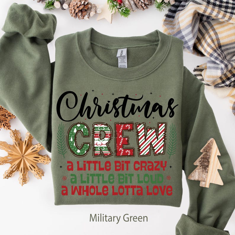 May include: Military green sweatshirt with the text "Christmas CREW" in a festive design. The word "CREW" is decorated with Christmas patterns and the phrases "a LITTLE BIT CRAZY", "a LITTLE BIT LOUD", and "a WHOLE LOTTA LOVE".