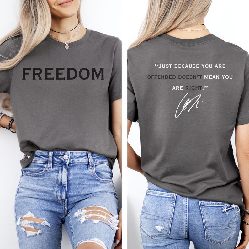 May include: A gray t-shirt with the word "FREEDOM" printed in large, black letters on the front. The back of the shirt features the quote, "JUST BECAUSE YOU ARE OFFENDED DOESN'T MEAN YOU ARE RIGHT." and a signature.