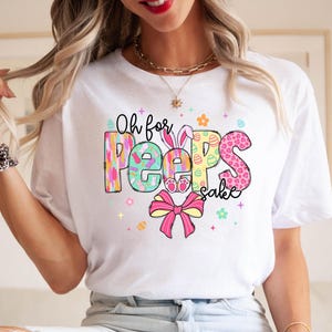 May include: White t-shirt with a colorful graphic that says "Oh for Peeps sake". The graphic features a bunny, eggs, and flowers.