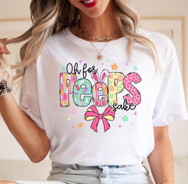 May include: White t-shirt with a colorful graphic that says "Oh for Peeps sake". The graphic features a bunny, eggs, and flowers.