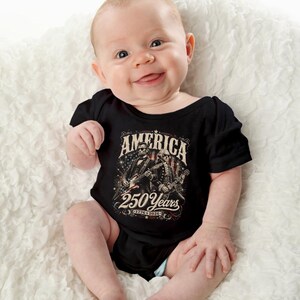May include: A smiling baby wearing a black onesie with the text "AMERICA 250 Years 1776-2026" and an illustration of two figures playing guitars. The baby is lying on a white, textured surface.
