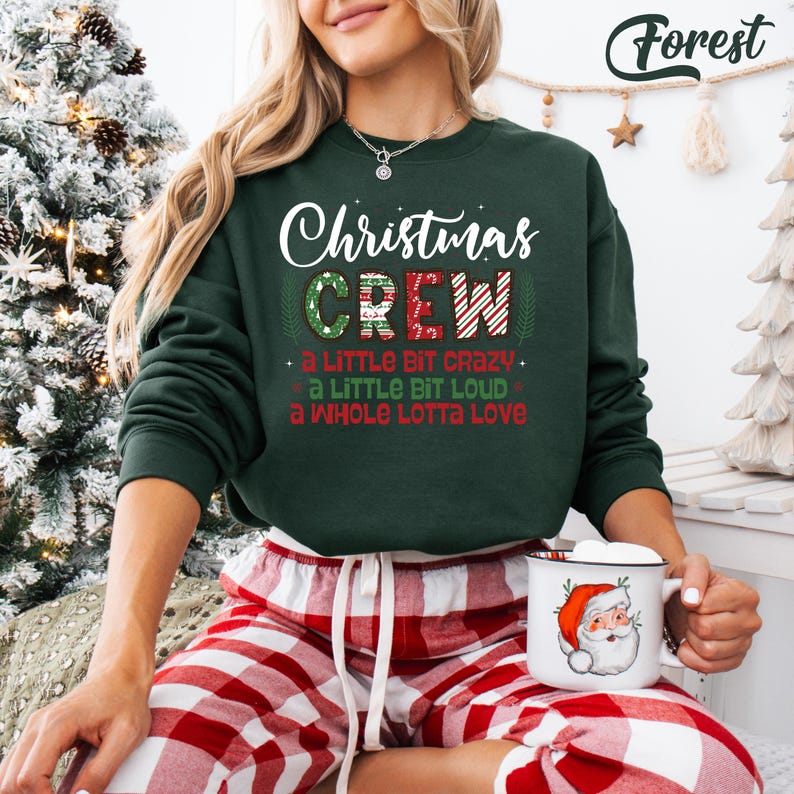 May include: A dark green Christmas sweatshirt with the words "Christmas CREW" in white and red. The sweatshirt also has the phrases "a LITTLE BIT CRAZY", "a LITTLE BIT LOUD", and "a WHOLE LOTTA Love". The person is wearing red and white plaid pajama pants.