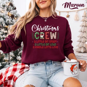 May include: Maroon Christmas Crew sweatshirt with white text. The design includes the words "Christmas Crew" and the phrases "a little bit crazy," "a little bit loud," and "a whole lotta love." The sweatshirt is a festive holiday apparel item.