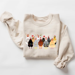 Peut inclure: Un sweat-shirt beige avec un motif de No&euml;l repr&eacute;sentant un groupe de poulets portant des bonnets de P&egrave;re No&euml;l et d&eacute;cor&eacute;s de lumi&egrave;res de No&euml;l.
