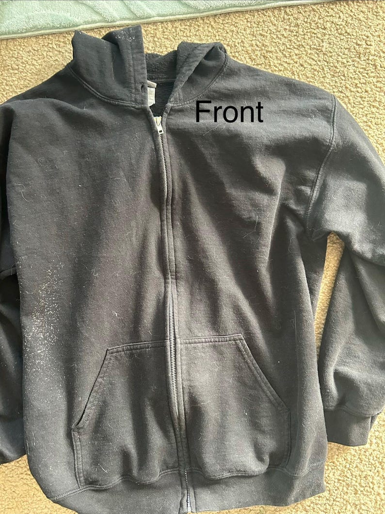 May include: A black zip-up hooded sweatshirt with a front pocket. The word "Front" is printed on the upper right side of the sweatshirt. The sweatshirt has a hood and a full-length zipper.