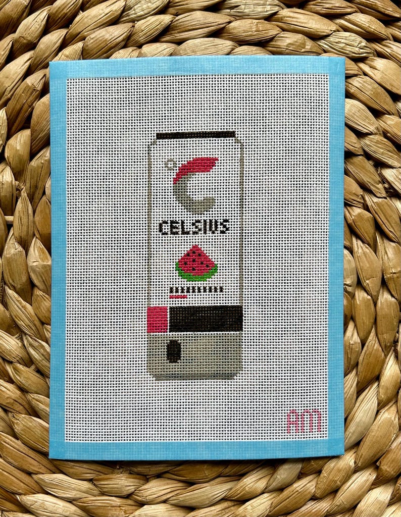 May include: A white and black can of Celsius energy drink with a watermelon design. The can has the text "Celsius" on it. The can is on a blue background with a pink "AM" in the bottom right corner.