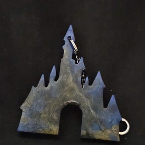 Könnte beinhalten: Ein blauer und grüner schlüsselanhänger in Form eines Schlosses mit einer silbernen Kette. Das Schloss hat ein detailliertes Design und einen Ausschnitt für den Schlüsselring.