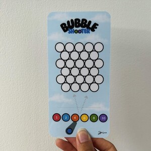 May include: A blue and white card with the text "BUBBLE SHOOTER" in black. The card has a grid of 35 white circles with black outlines. There are numbers 1 through 10 in coloured circles at the bottom of the card.