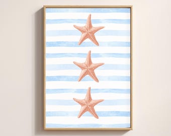 May include: A framed print featuring three coral-colored starfish on a background of blue and white horizontal stripes. The artwork is encased in a light brown wooden frame, creating a coastal or nautical theme.
