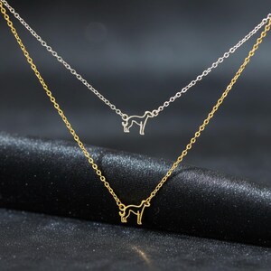 May include: Two-layered necklace featuring a dog silhouette pendant. The top chain is silver, and the bottom chain is gold. The dog pendant is a simple outline, adding a touch of elegance to the jewelry.